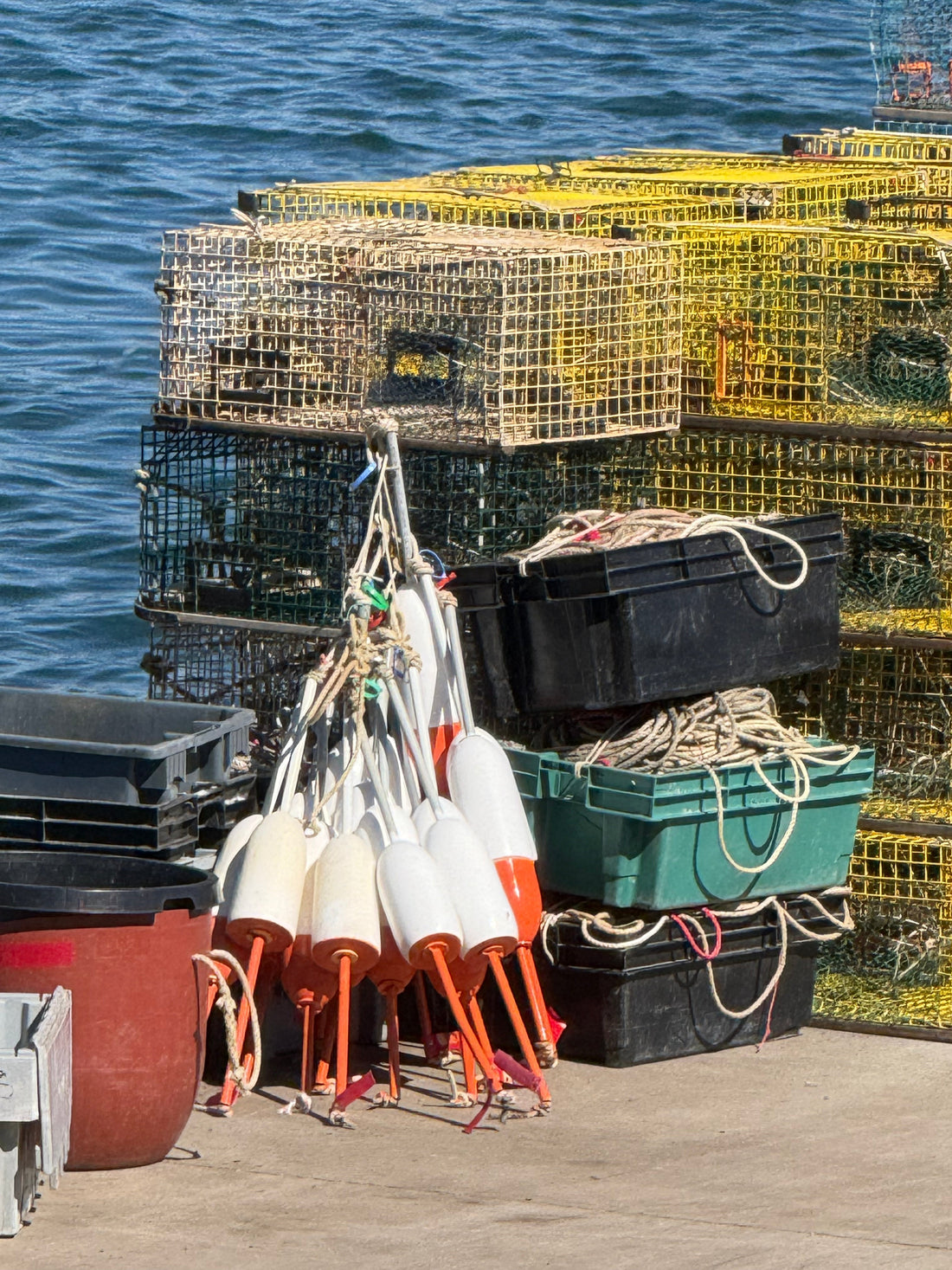 A photo of lobster traps and buoys stacked up on a dock with choppy waves in the background. 